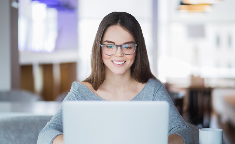 Portrait of cheerful student using laptop in cafe