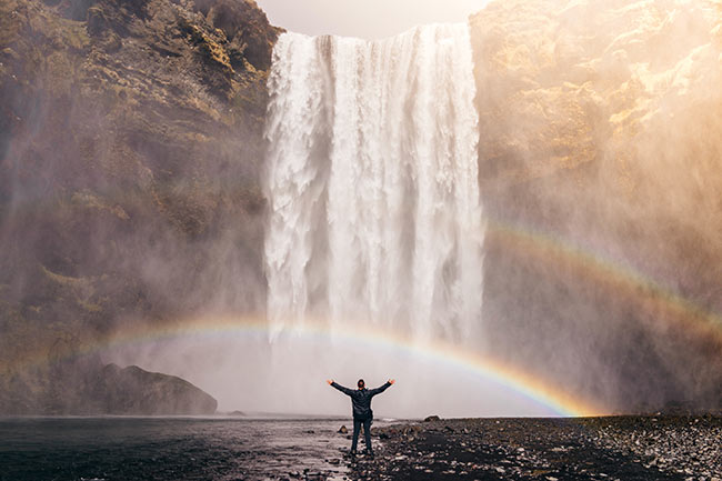 man standing before a waterfall with hands spread apart