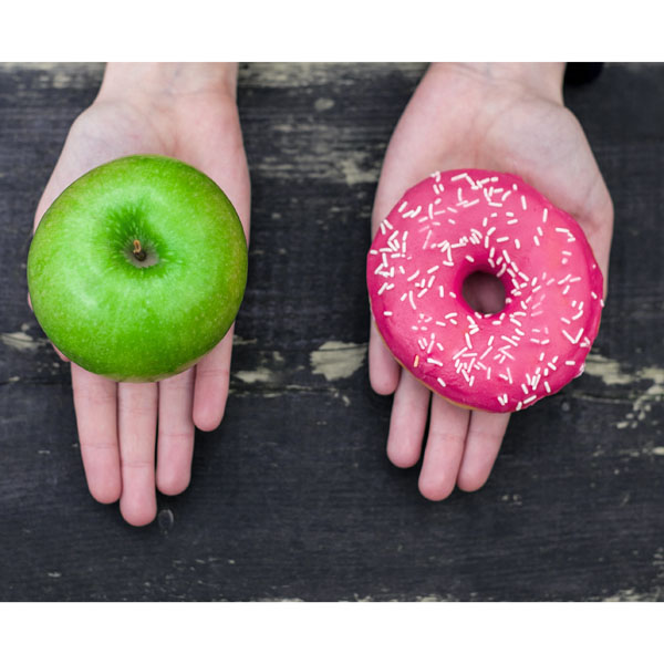 two hands holding an apple and a pink donut with sprinkles