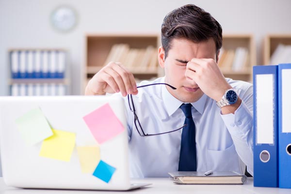 confused young man sitting in front of computer rubbing his eyes