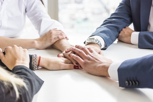 four team members with their hands on top of each other in the middle of table i