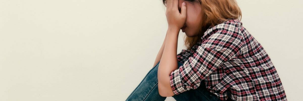 young hipster woman, sad, long-haired sitting hugging legs.