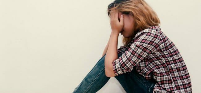 young hipster woman, sad, long-haired sitting hugging legs.
