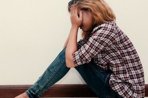 Young hipster woman, sad, long-haired sitting hugging legs.