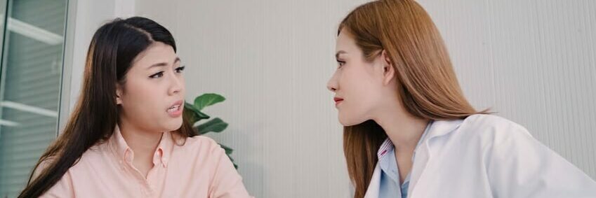 Doctor talking to unhappy teenage patient in exam room. Asian wo
