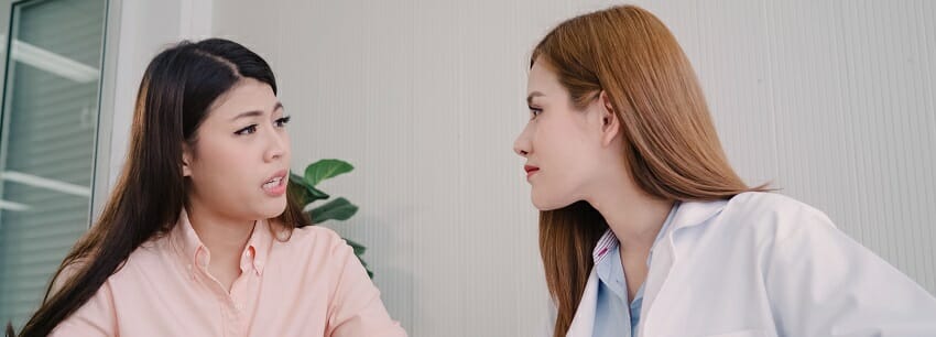 Doctor talking to unhappy teenage patient in exam room. Asian wo