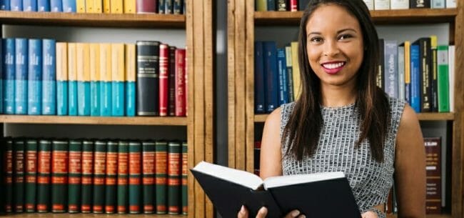 565210-PL5QYE-92a Young woman holding a book in front of bookshelf