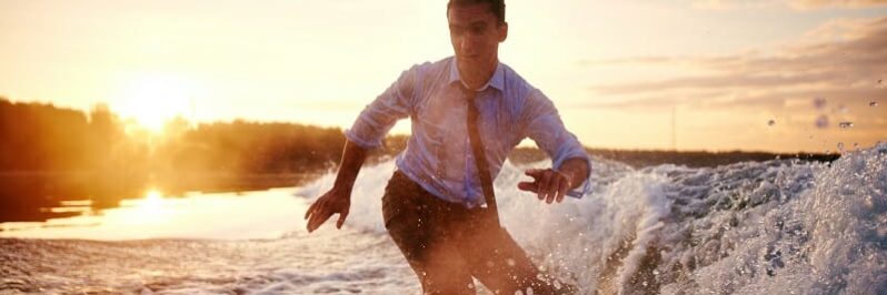 Young man in wet clothes surfboarding at summer resort