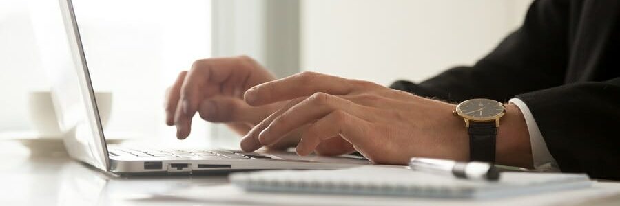 Close up image of mans hands in wristwatch typing on laptop