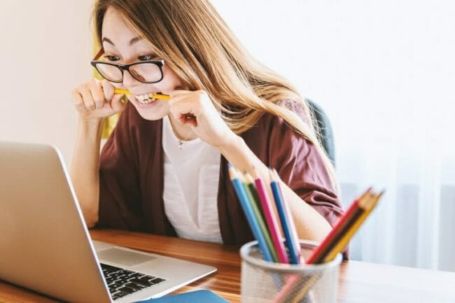 Young woman sitting in front of computer bitting pencil in frustration