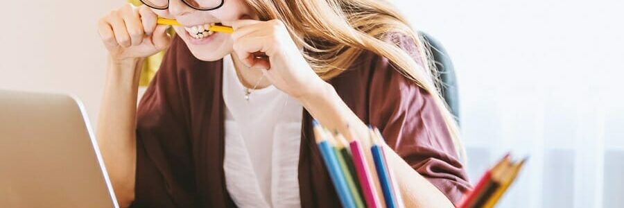 quiz (2) Young woman sitting in front of computer bitting pencil in frustration