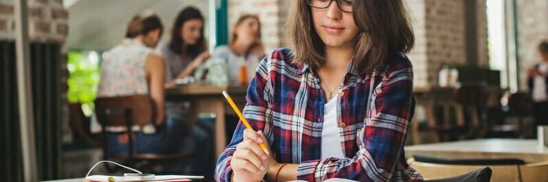 Young woman sitting alone studying with pencil in hand