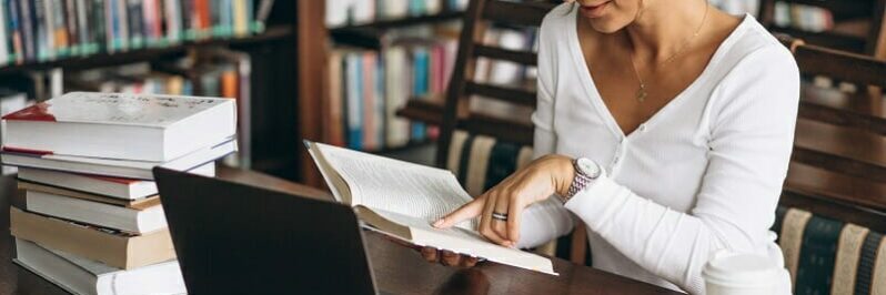 Young woman sitting at the library using books and computer