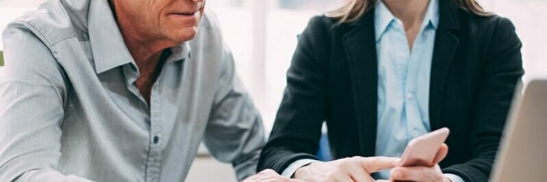 Smiling businesswoman showing phone to colleague