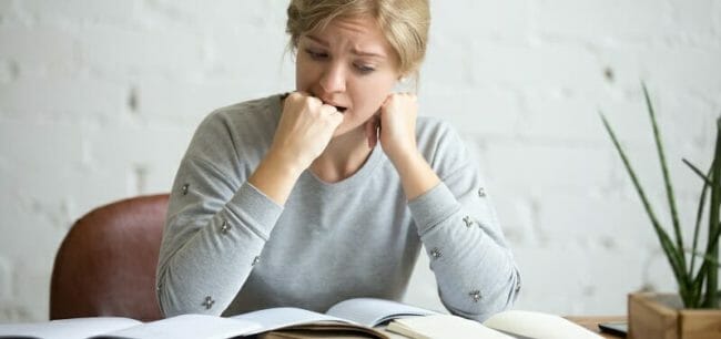 Portrait of a student girl sitting at the desk biting her fist