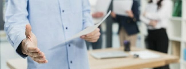 man holding paper in one hand, the other hand is extended for a handshake man holding paper in one hand, the other hand is extended for a handshake