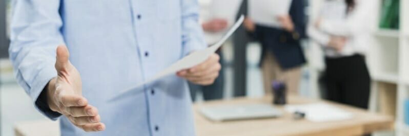 man holding paper in one hand, the other hand is extended for a handshake