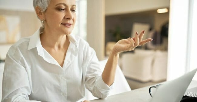 Portrait of energetic successful mature businesswoman in white shirt having online business meeting via video conference call, gesturing emotionally, discussing agreement, sitting at desk with laptop