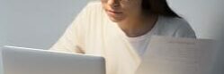 Millennial manager in glasses working on laptop and holding docu