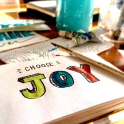 desk top with a page with written words that states Choose JOY in colorful letters